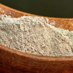 A wooden bowl filled with a fine powder, likely a spice or herb, resting on a wooden surface