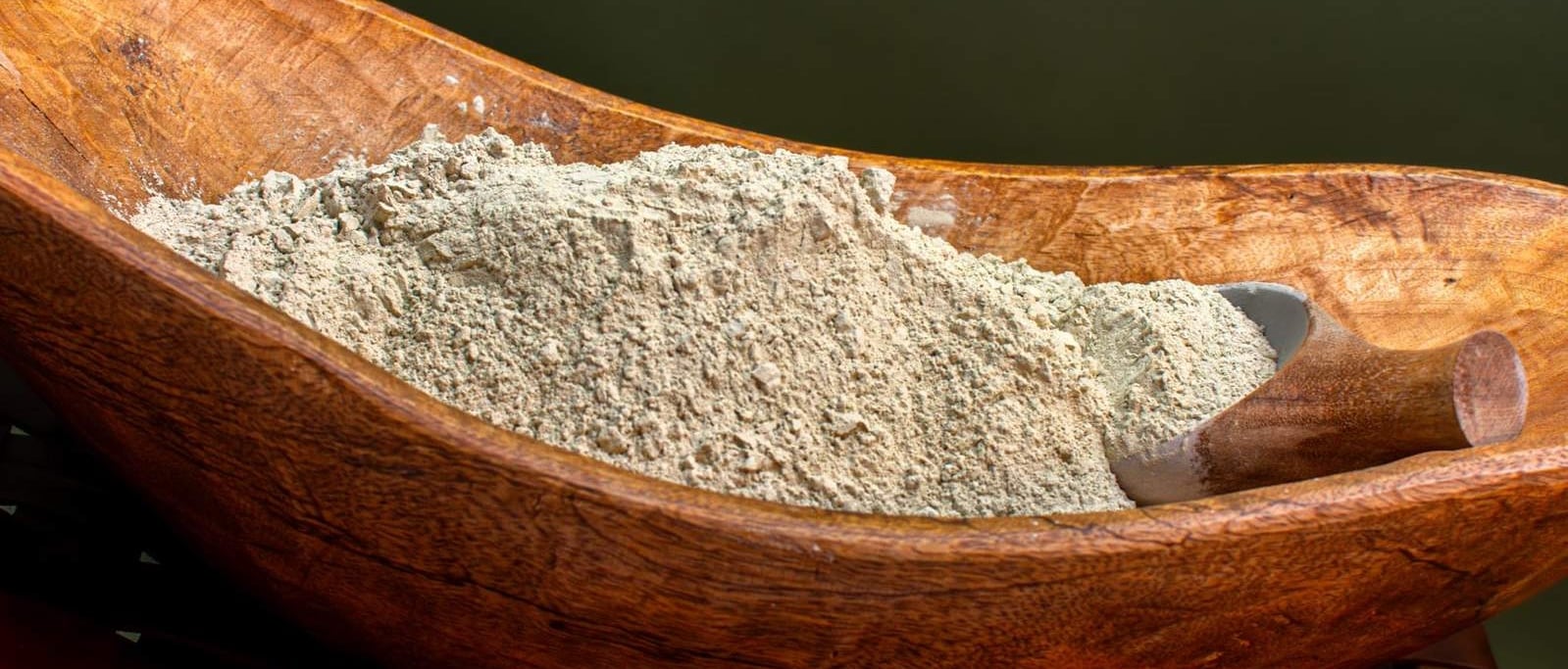 A wooden bowl filled with a fine powder, likely a spice or herb, resting on a wooden surface