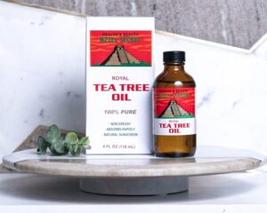 An image showing a bottle of Royal Tea Tree Essential Oil, a health and beauty product, on a table with some greenery.