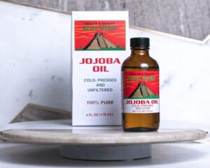 A bottle of Jojoba Essential Oil and its packaging on a marble surface.