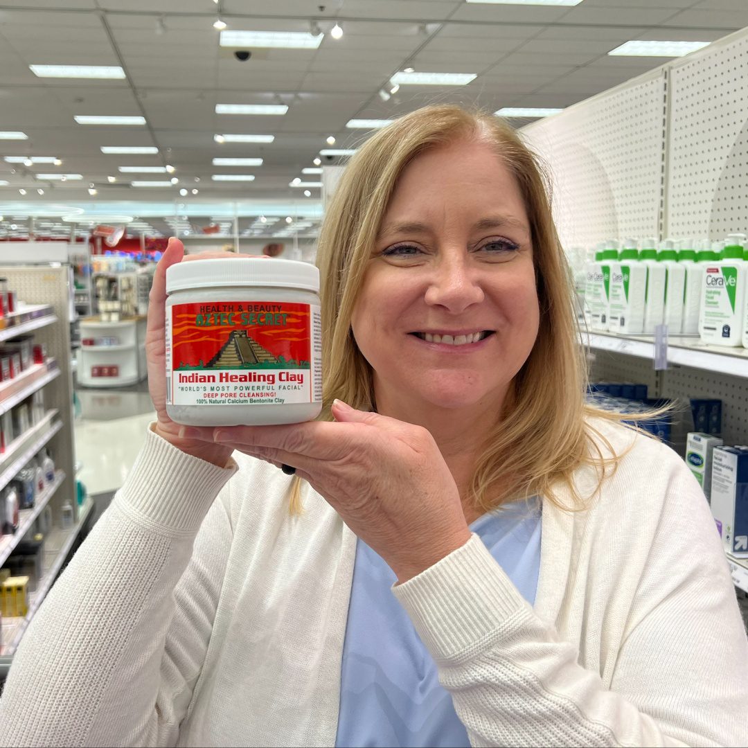 An image showing a smiling woman holding a jar of Indian Healing Clay in a store aisle.