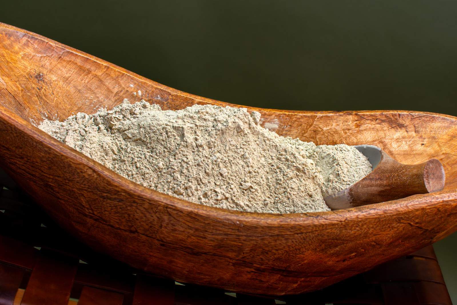 A wooden spoon in a glass bowl filled with a white powdery substance on a wooden surface